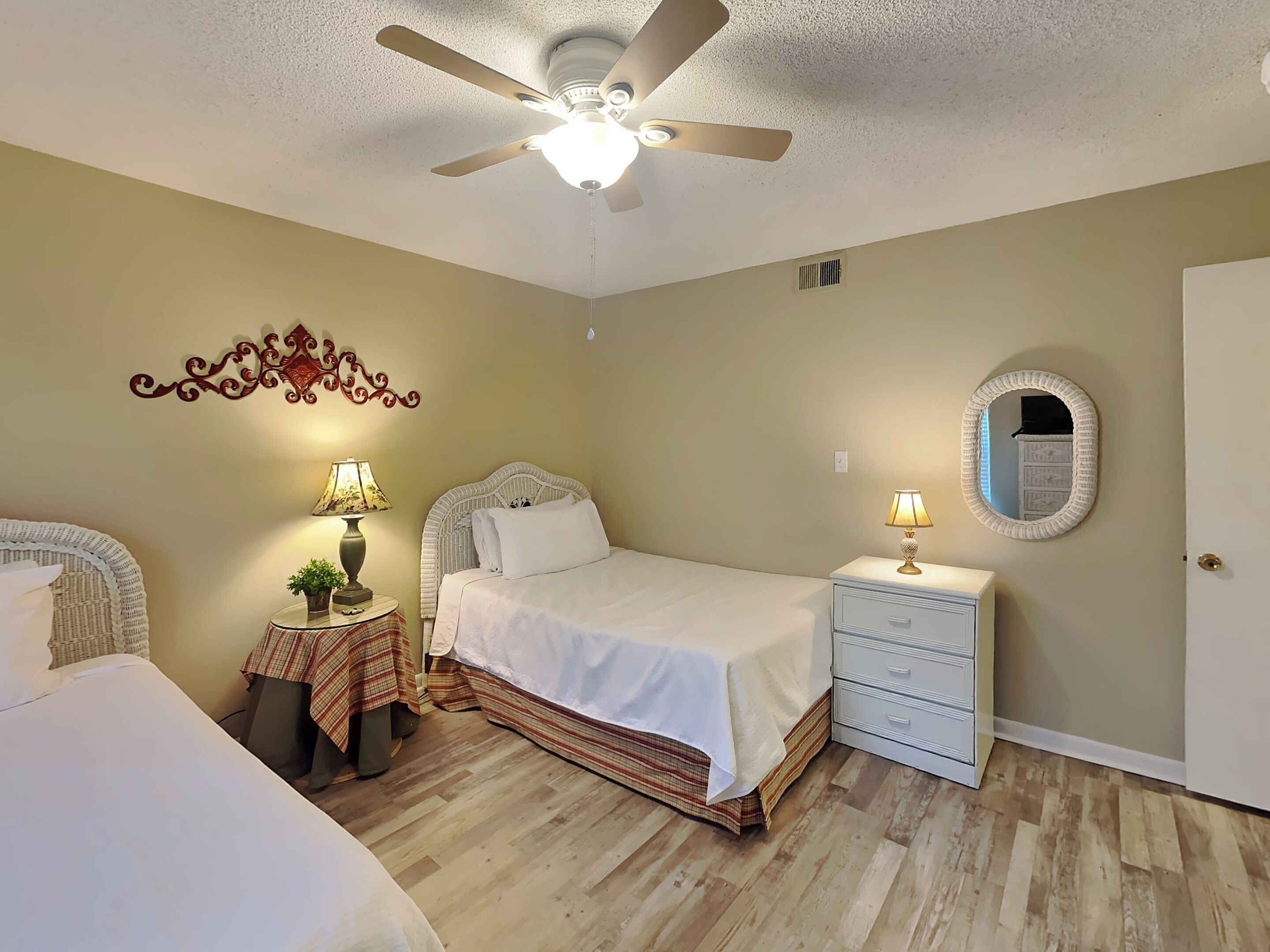 Une chambre à coucher comprenant un lit, des tables de chevet, un ventilateur de plafond, un miroir et un élément décoratif mural.