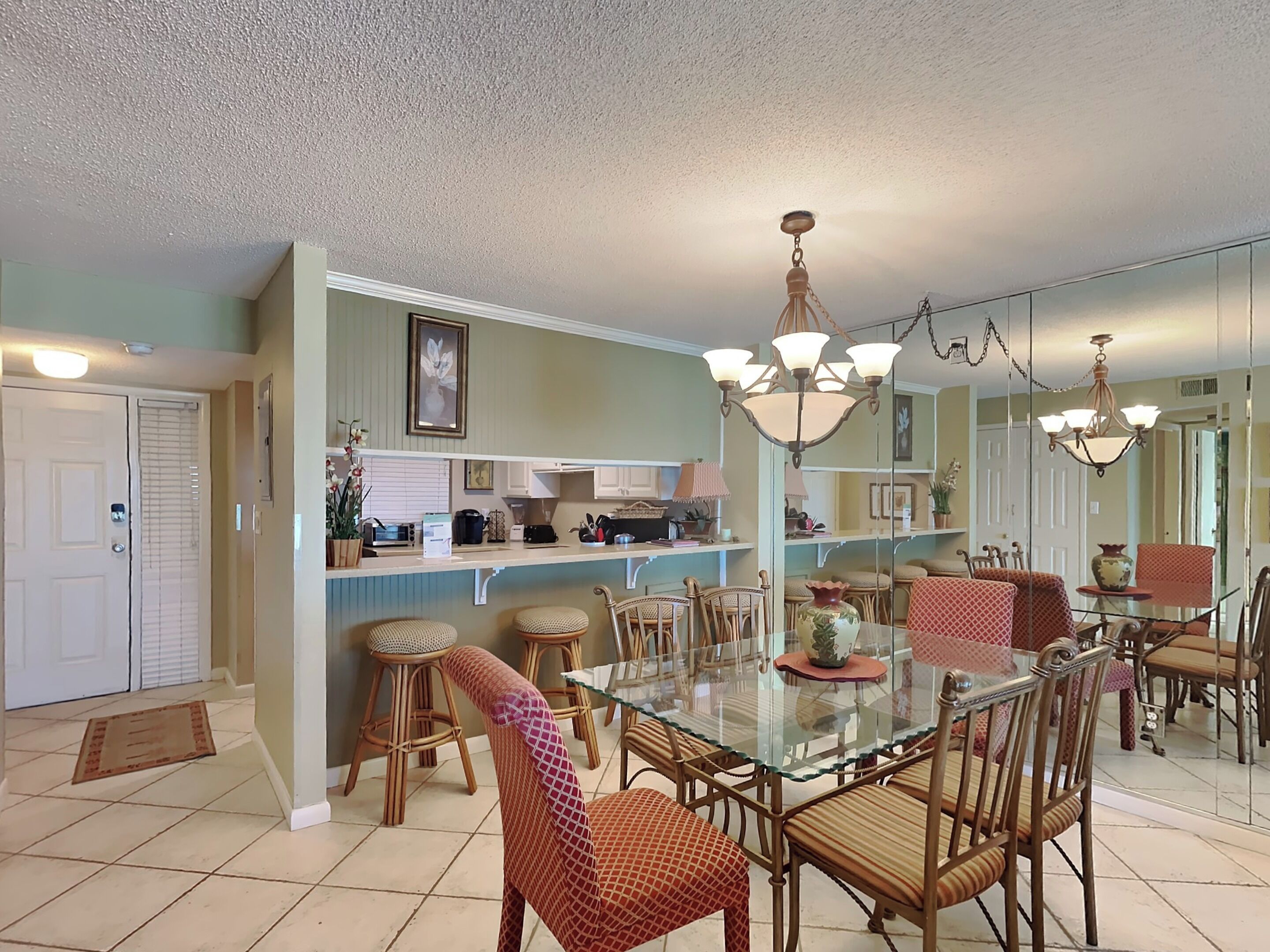 A dining area with a glass table, wicker chairs, and a kitchen in the background.