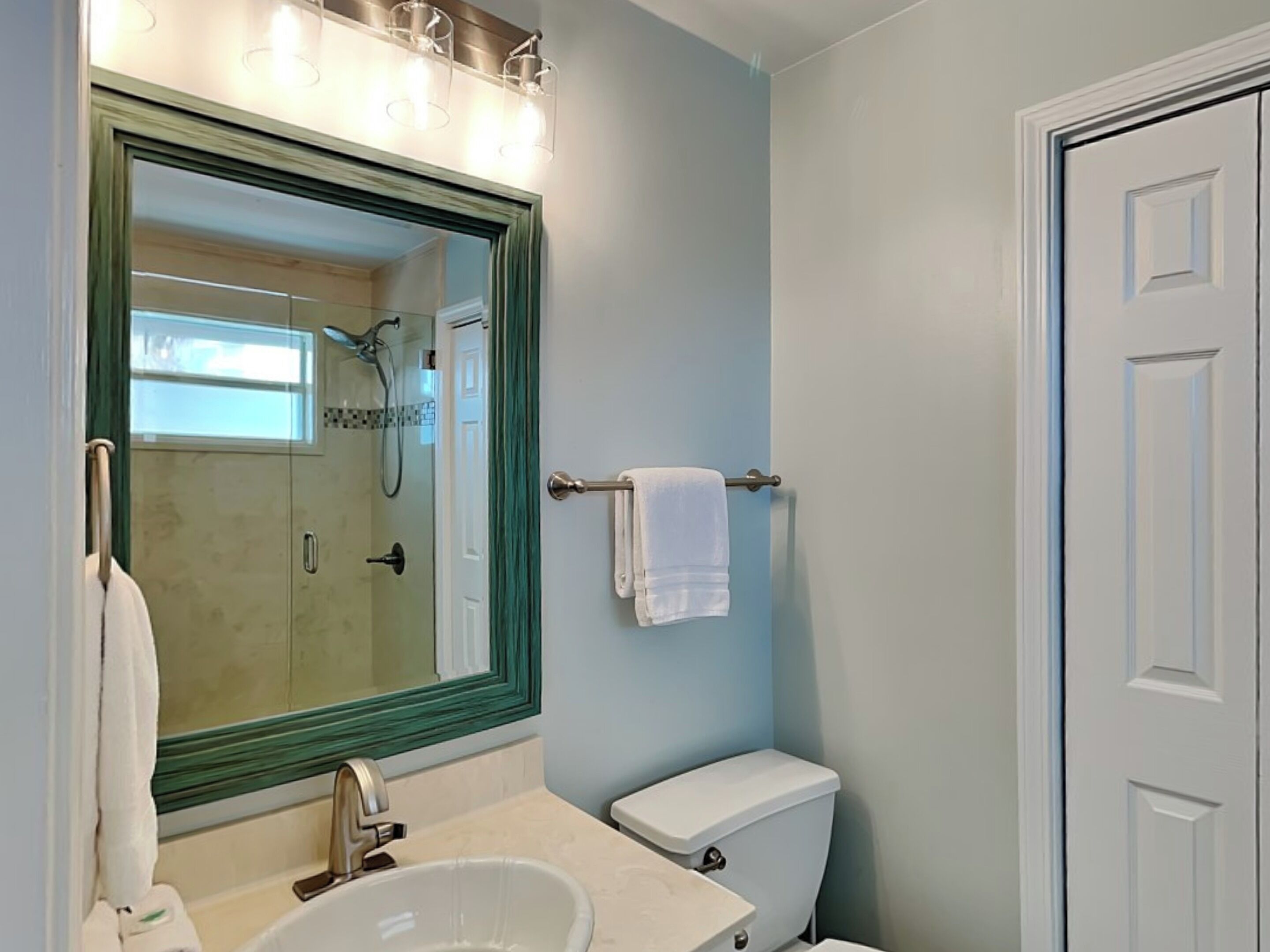 A bathroom with a large mirror, a sink, a toilet, and a shower area.