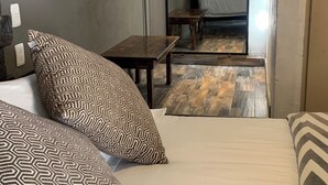 Une chambre d’hôtel avec un lit, des coussins à motifs, une petite table et un miroir qui reflète la pièce.