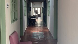 Un couloir avec un sol carrelé, des portes vertes et une chaise rose.