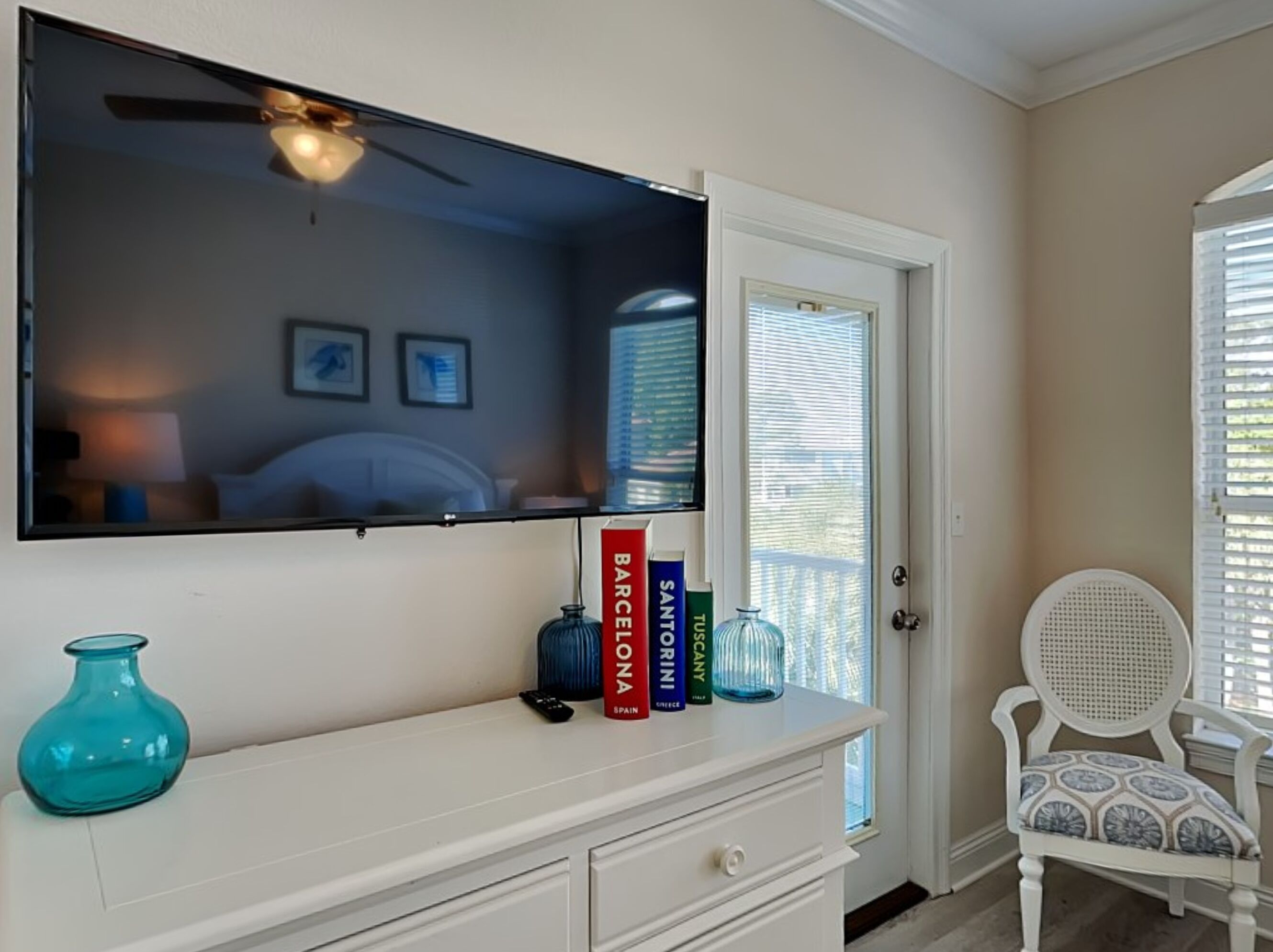 Ein Hotelzimmer mit einem großen Flachbildfernseher über einem weißen Schminktisch, einem Deckenventilator und einer Tür mit Fenster.