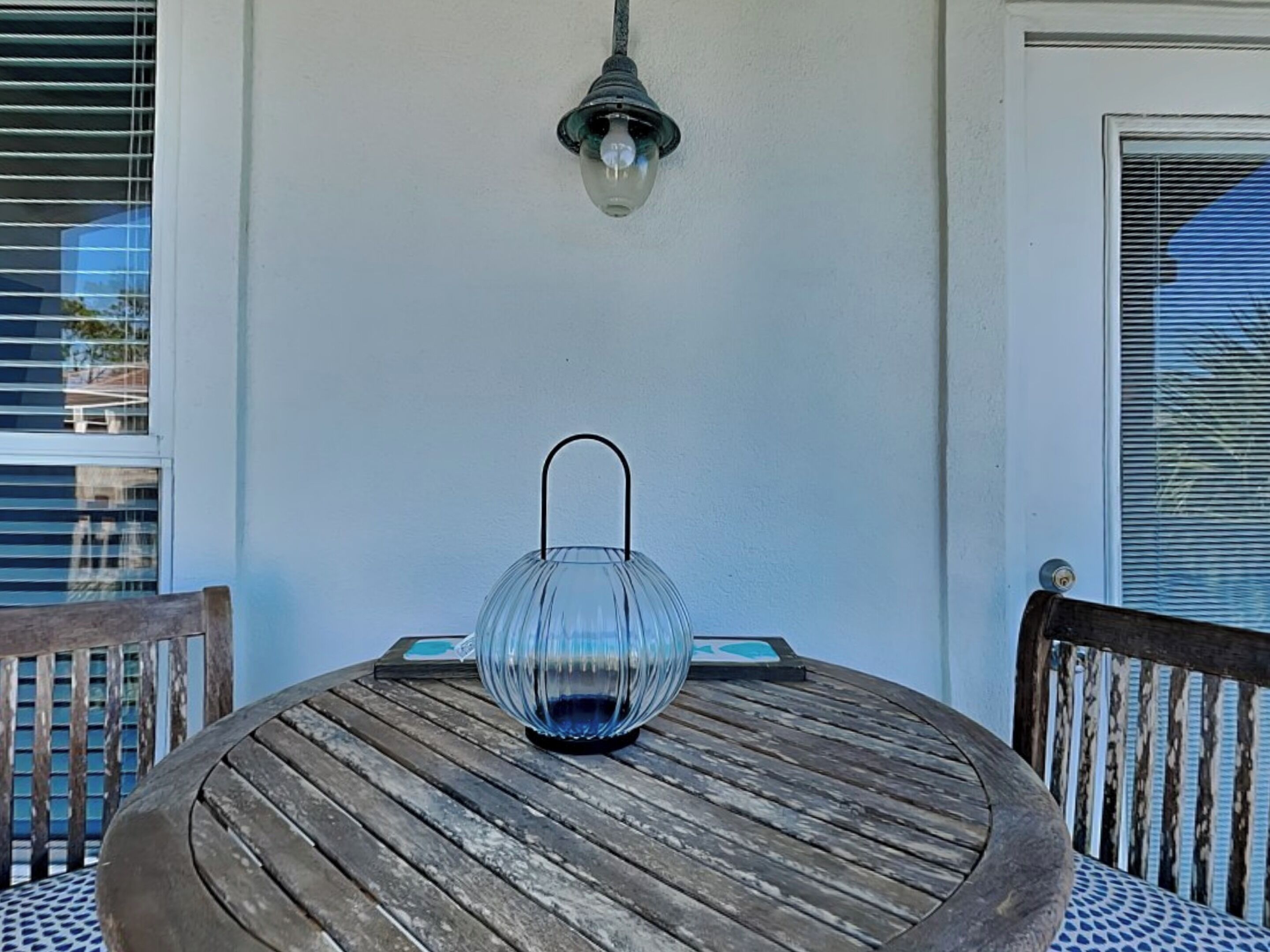 A round wooden table with a glass lantern in the center, a wall-mounted light fixture above, and a door with a window on the right.
