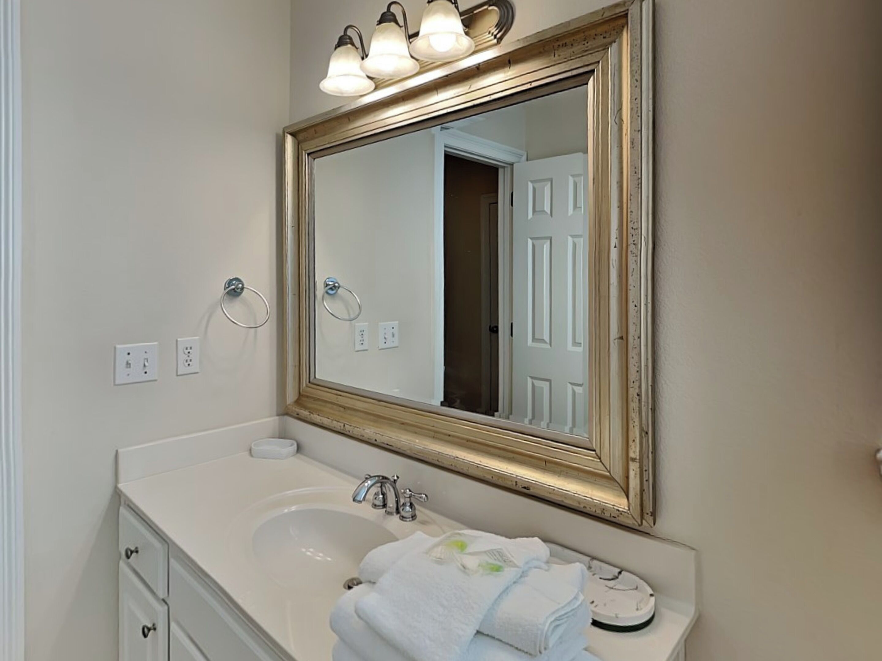 Une salle de bain avec un lavabo blanc, un miroir avec un cadre doré et un porte-serviettes.