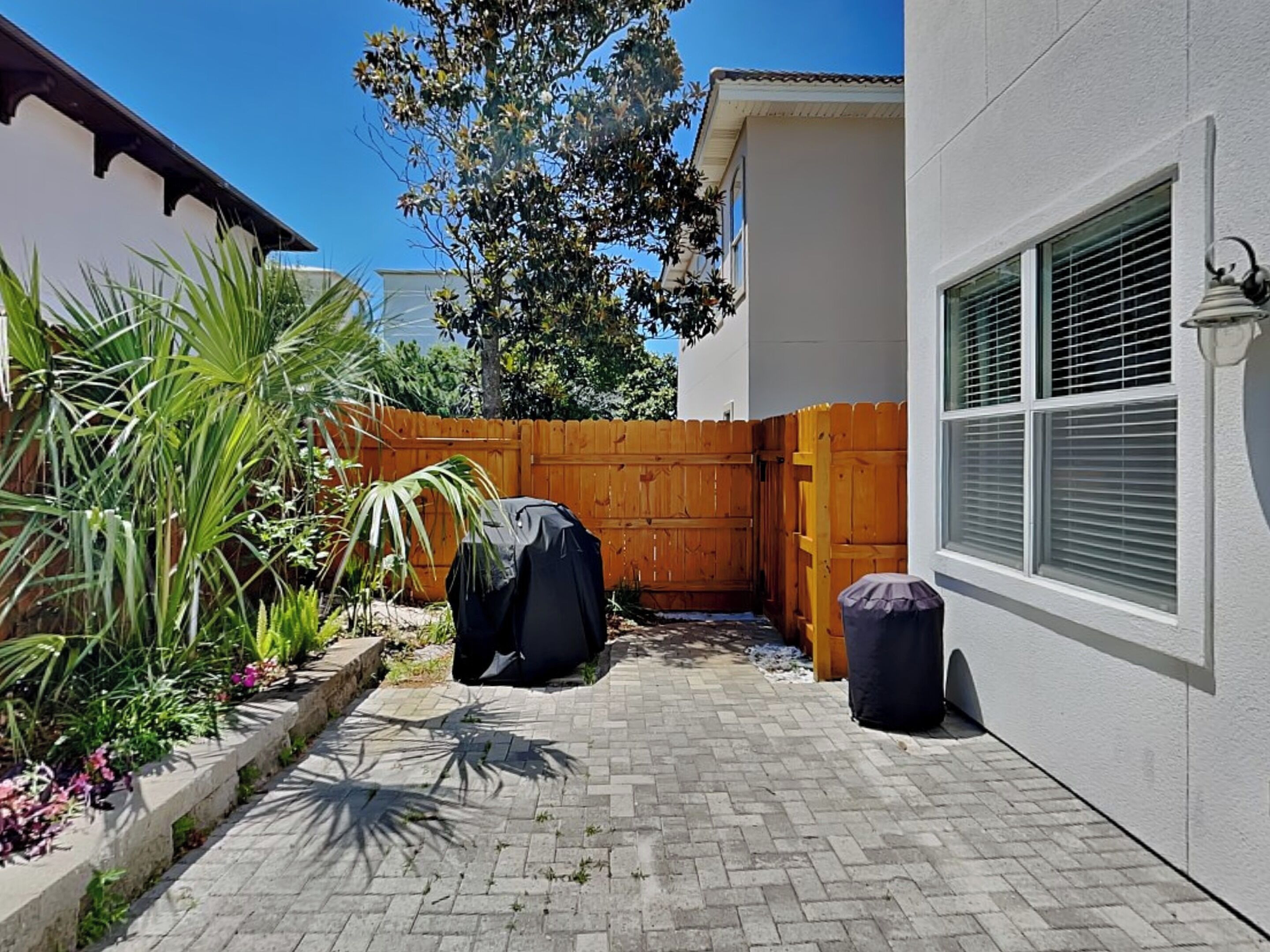 A backyard with a brick patio, a wooden fence, and a covered grill.