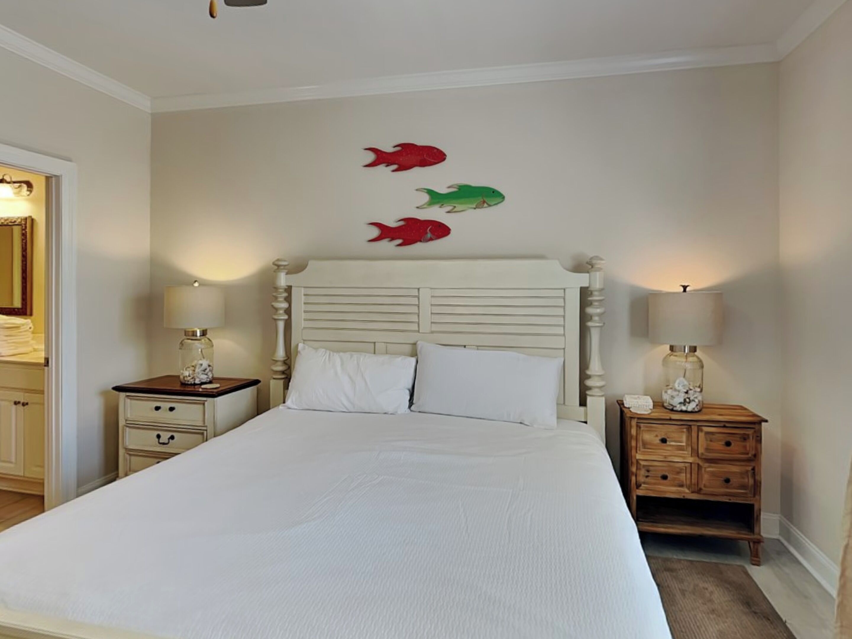 Un dormitorio con una cama grande, dos mesitas de noche con lámparas y una pared decorada con tres adornos de peces.
