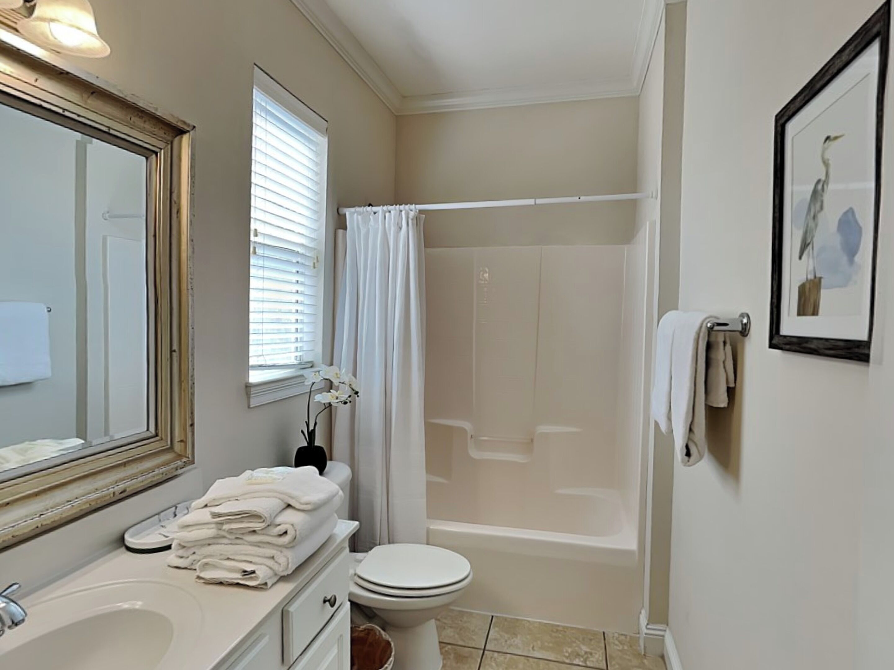 A bathroom with a sink, toilet, and bathtub. There is a window with blinds, a towel rack, and a framed picture on the wall.