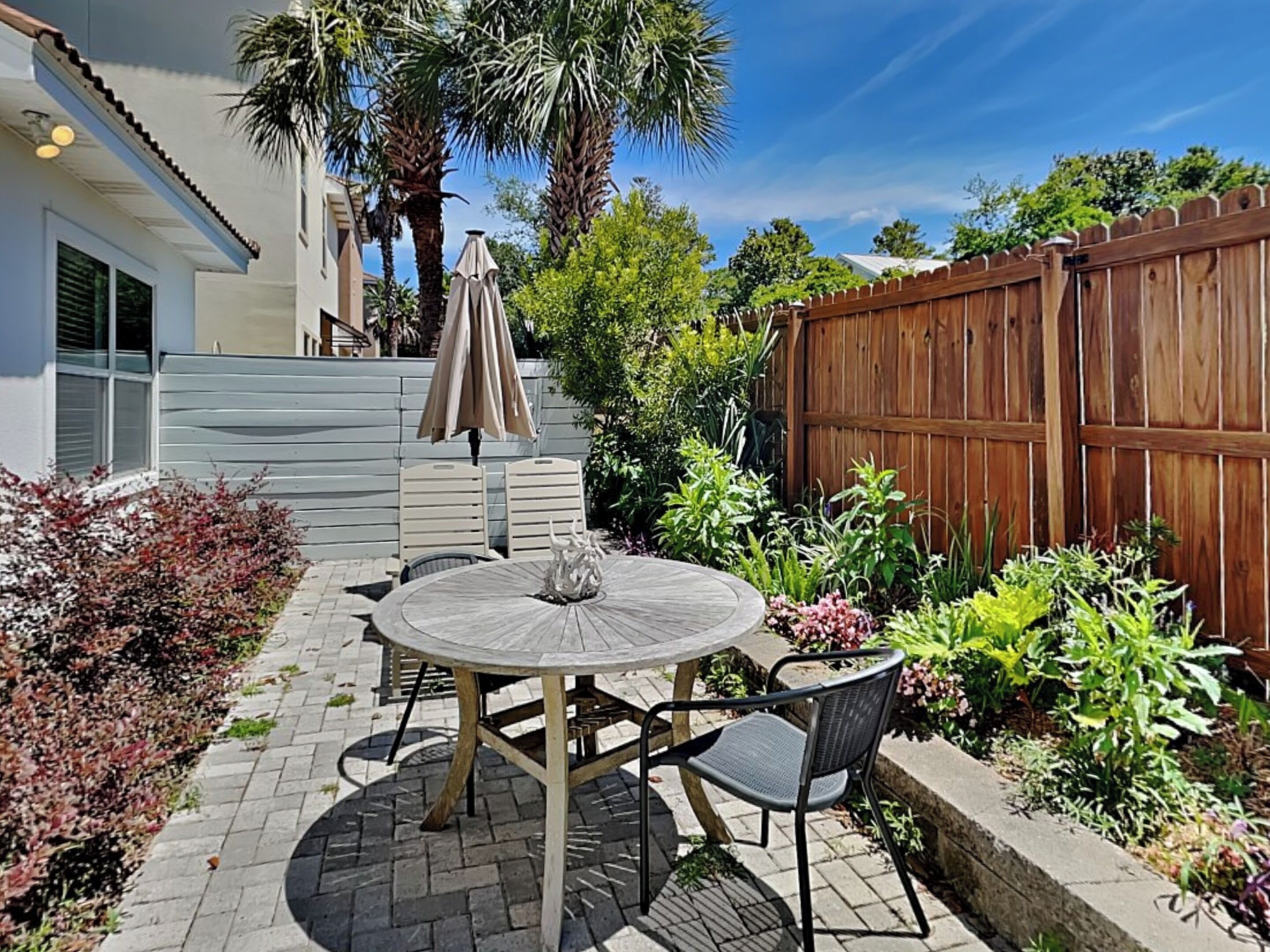 A patio with a round table and chairs, surrounded by a wooden fence and various plants.