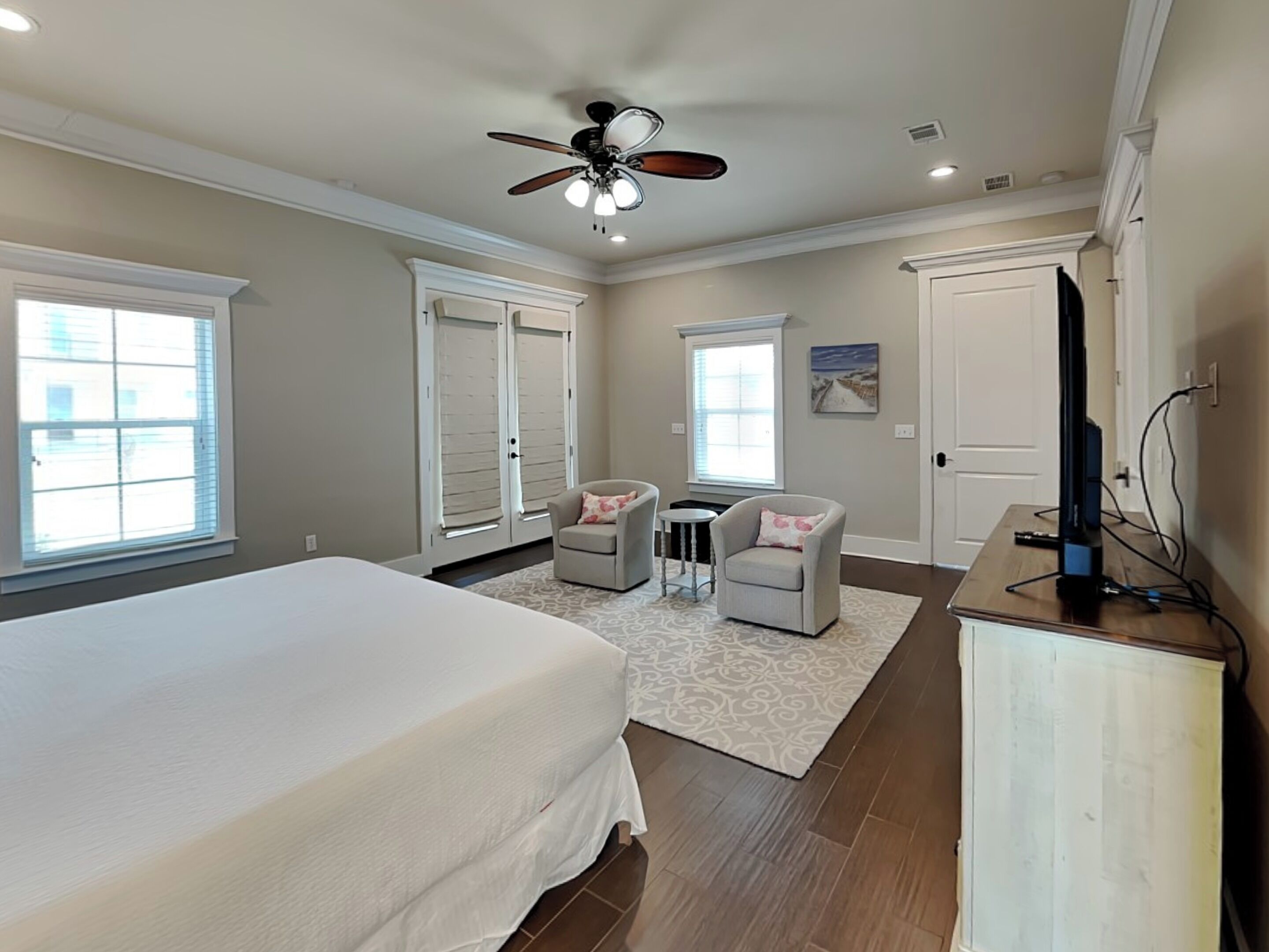 A bedroom with a bed, two chairs, a desk with a TV, and a ceiling fan.