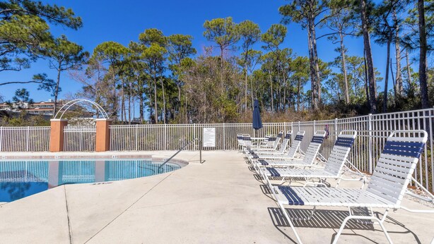 A pool area with lounge chairs and a fence.