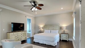 A bedroom with a large bed, a television, a ceiling fan, and a small table. - Frangista Sanctuary by Southern Vacation Rentals (Miramar Beach)