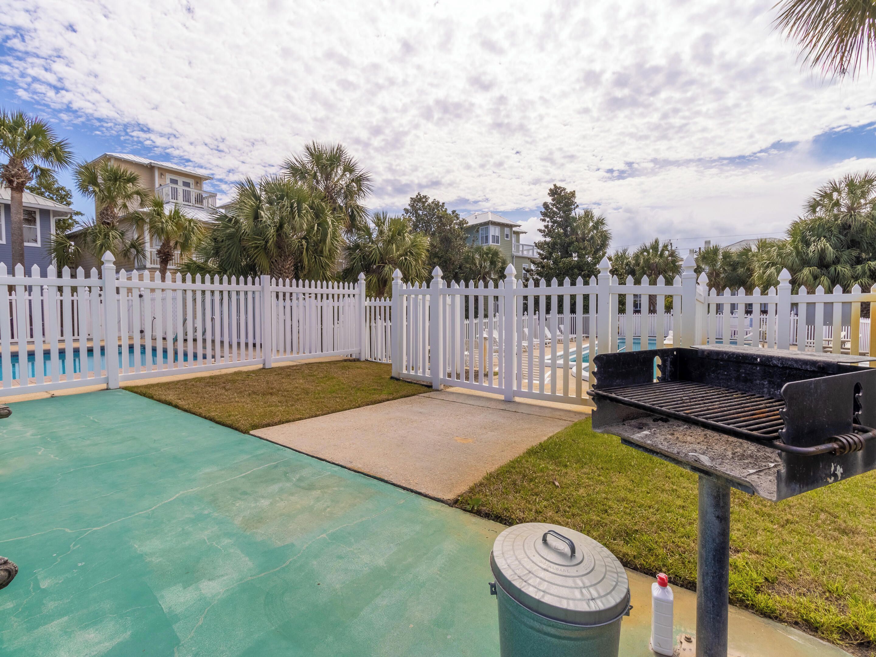 A backyard with a pool, a barbecue grill, and a white picket fence.