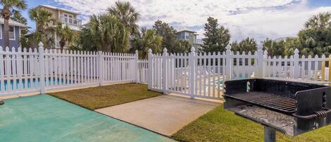 A backyard with a pool, a barbecue grill, and a white picket fence.