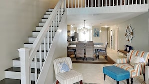 A spacious living area with a staircase, a dining area, and a view of the kitchen. - Palms North #7B by Southern Vacation Rentals (Santa Rosa Beach)