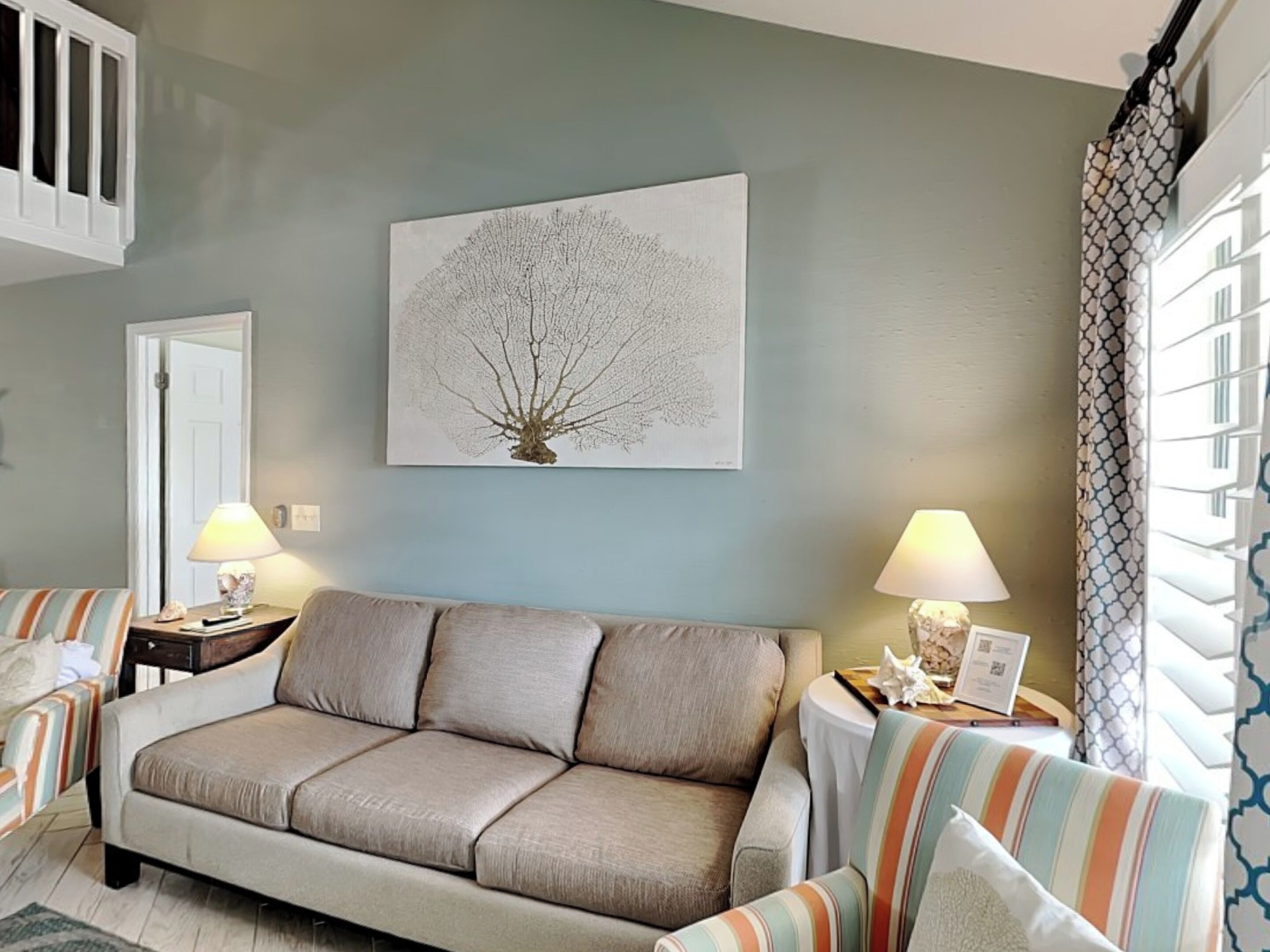 A living room with a beige sofa, striped armchairs, and a wall-mounted tree artwork.