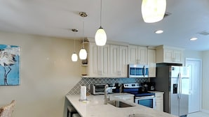 A modern kitchen with white cabinets, a large island with stools, stainless steel appliances, and pendant lighting. - Palms North #7B by Southern Vacation Rentals (Santa Rosa Beach)
