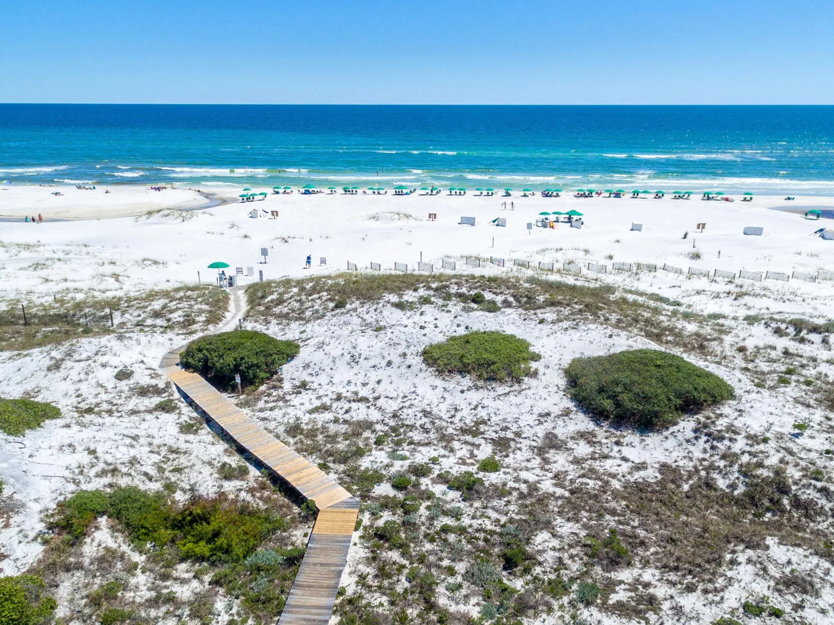 A beach with a wooden boardwalk leading to the shore, surrounded by sand and sparse vegetation.