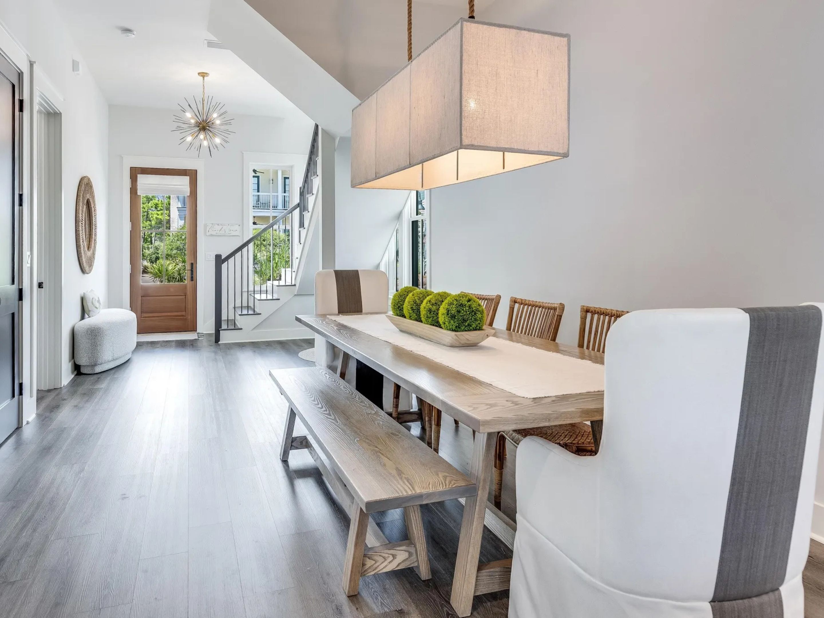 A modern dining area with a wooden table, benches, and a hanging light fixture.