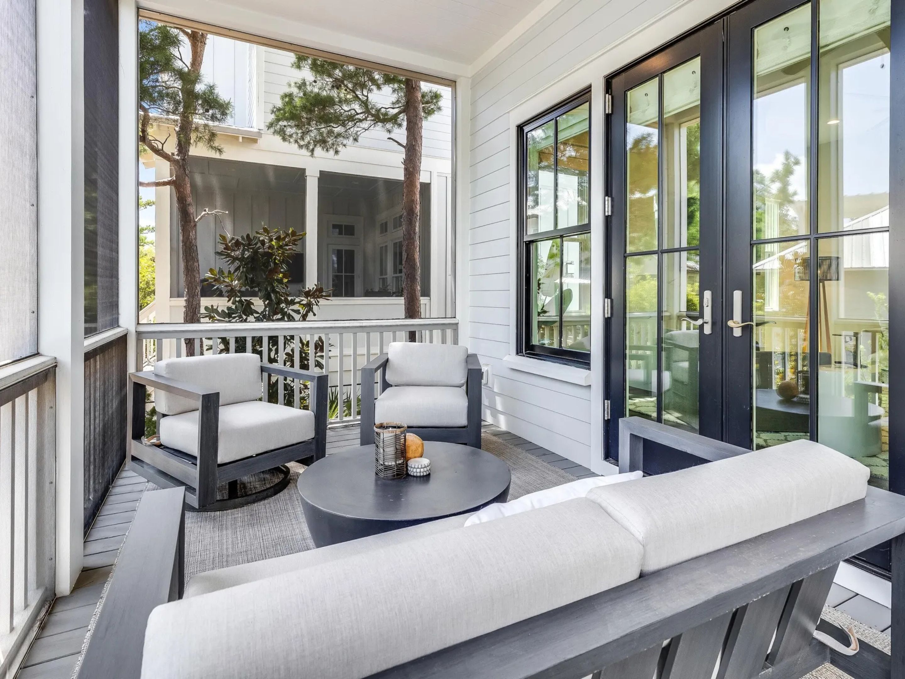 A covered porch with two cushioned chairs, a round table, and a bench.
