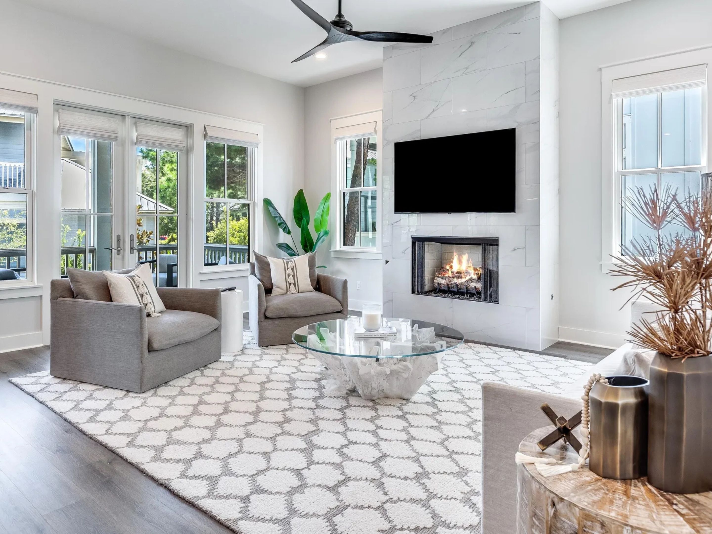 A modern living room with a fireplace, large windows, and a ceiling fan.