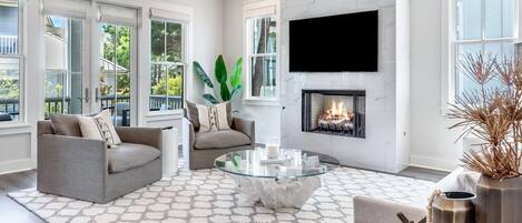 A modern living room with a fireplace, large windows, and a ceiling fan.