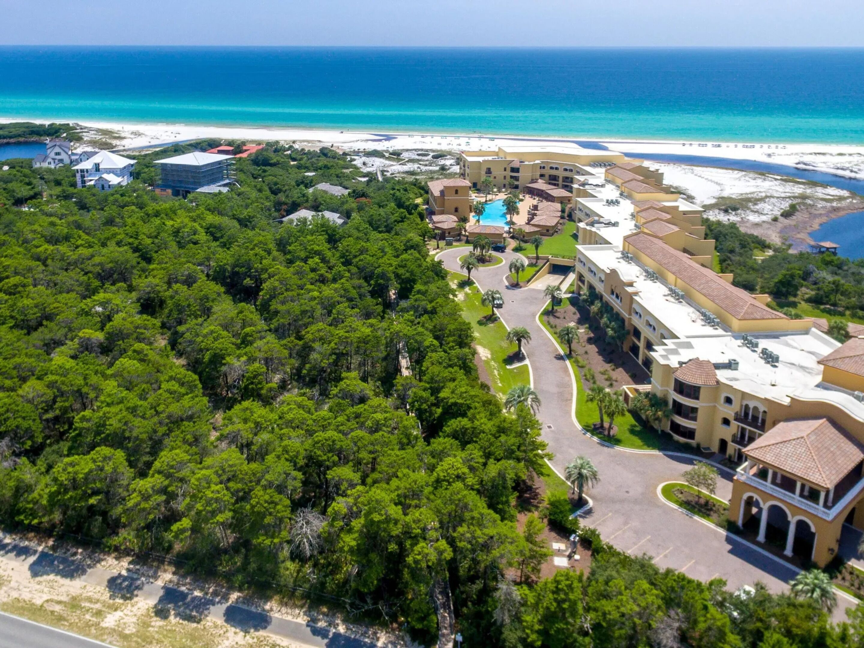 An aerial view of a resort with a pool, beachfront, and dense greenery.