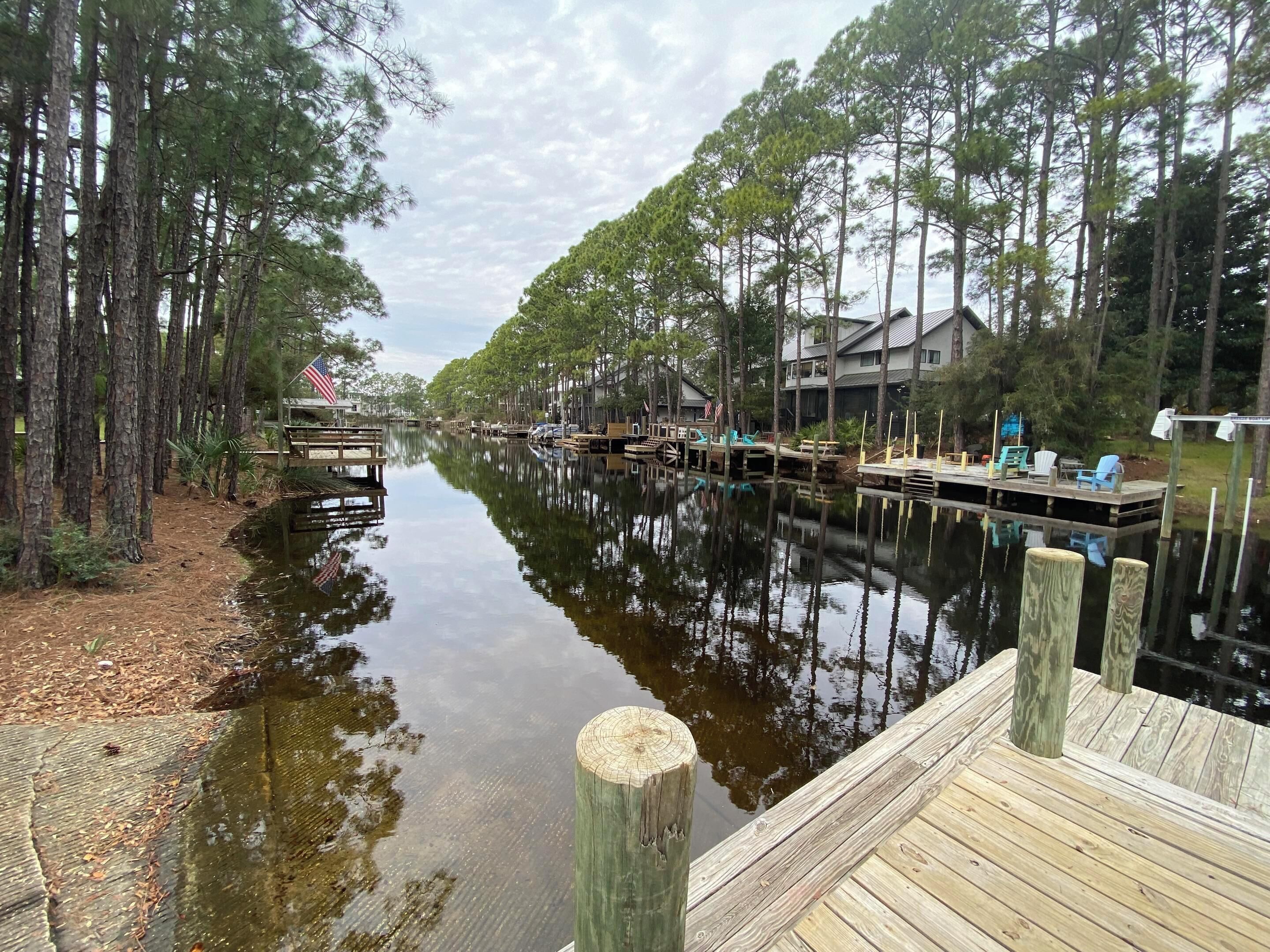 A calm waterway flanked by tall trees and wooden docks with chairs and tables.