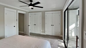 Een slaapkamer met een bed, een plafondventilator en een grote schuifdeur met glas aan de rechterkant.