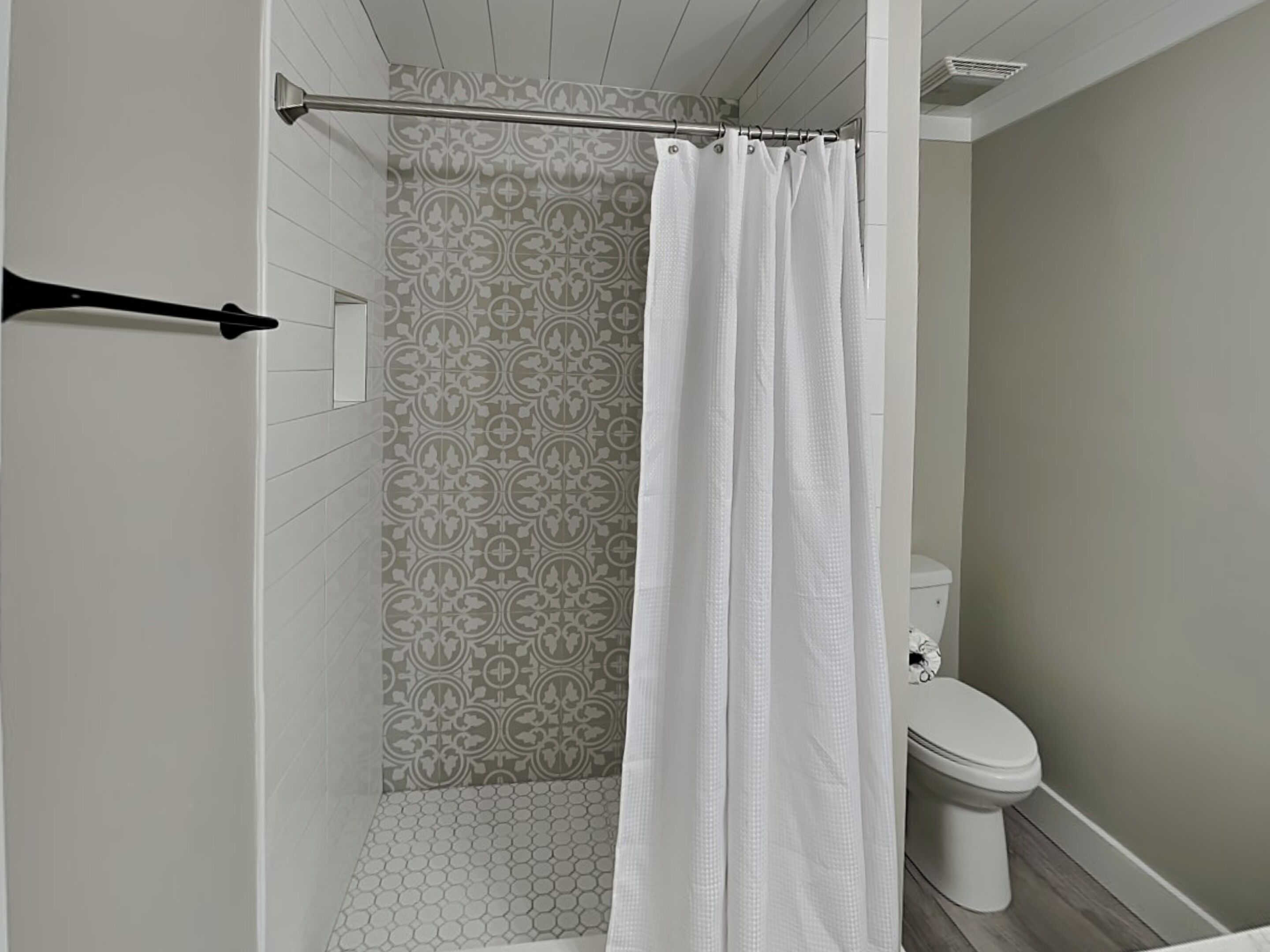 Uma casa de banho moderna com chuveiro, sanita e azulejos estampados.
