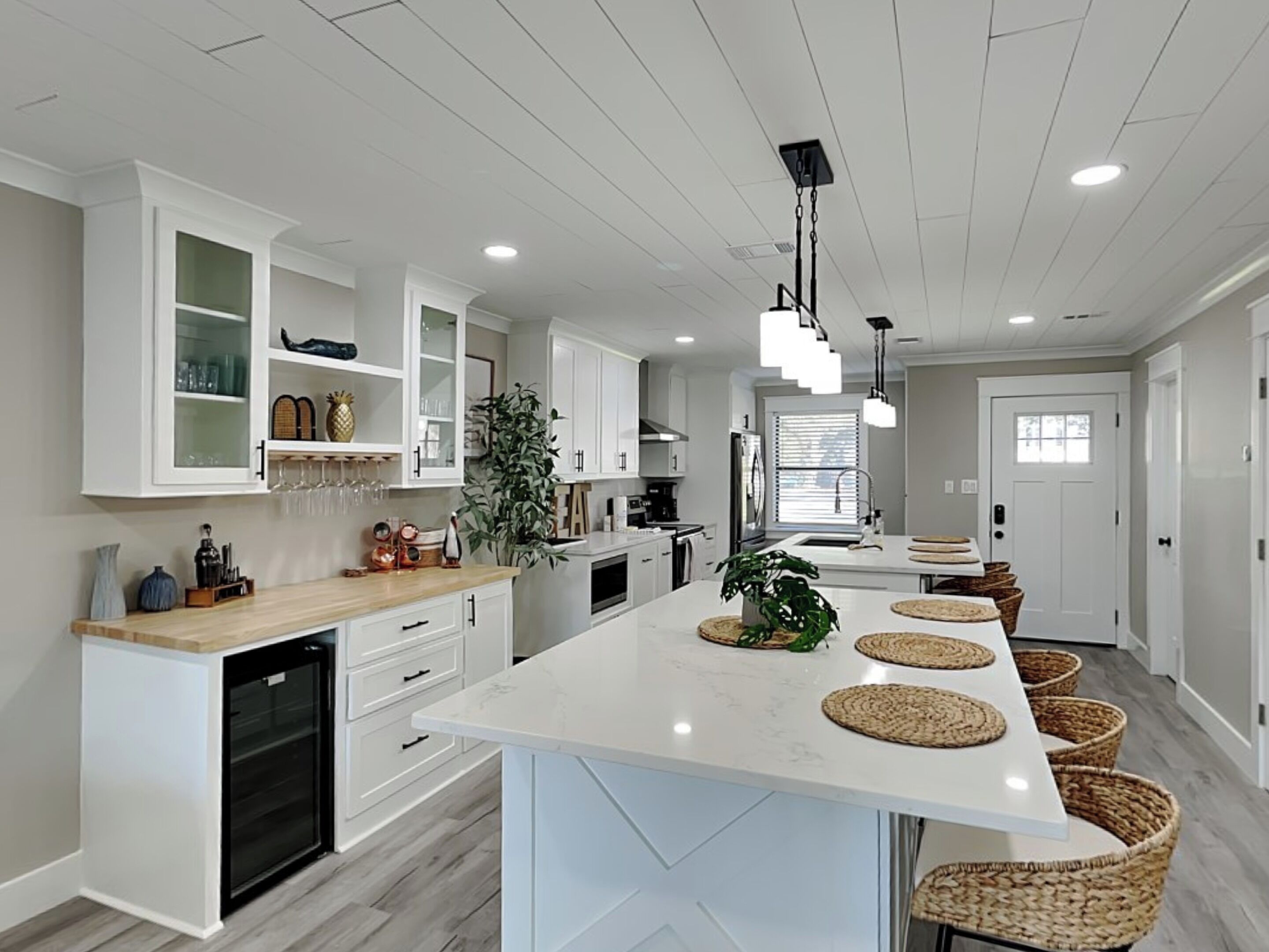 A modern kitchen with white cabinetry, a central island with woven placemats, and a built-in dishwasher.