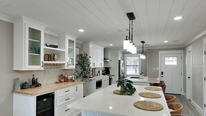 Een moderne keuken met witte kastjes, een centraal eiland met geweven placematen en een inbouw vaatwasser.