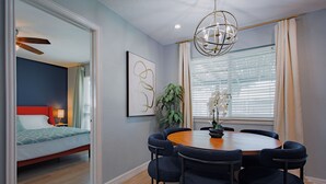 A modern dining area with a round table and six upholstered chairs, a ceiling fan, and a large window with blinds.