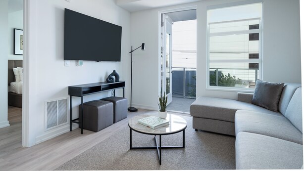 Ein modernes Wohnzimmer mit Flachbildfernseher, einer Couch, einem Couchtisch und einem Balkon mit Aussicht.