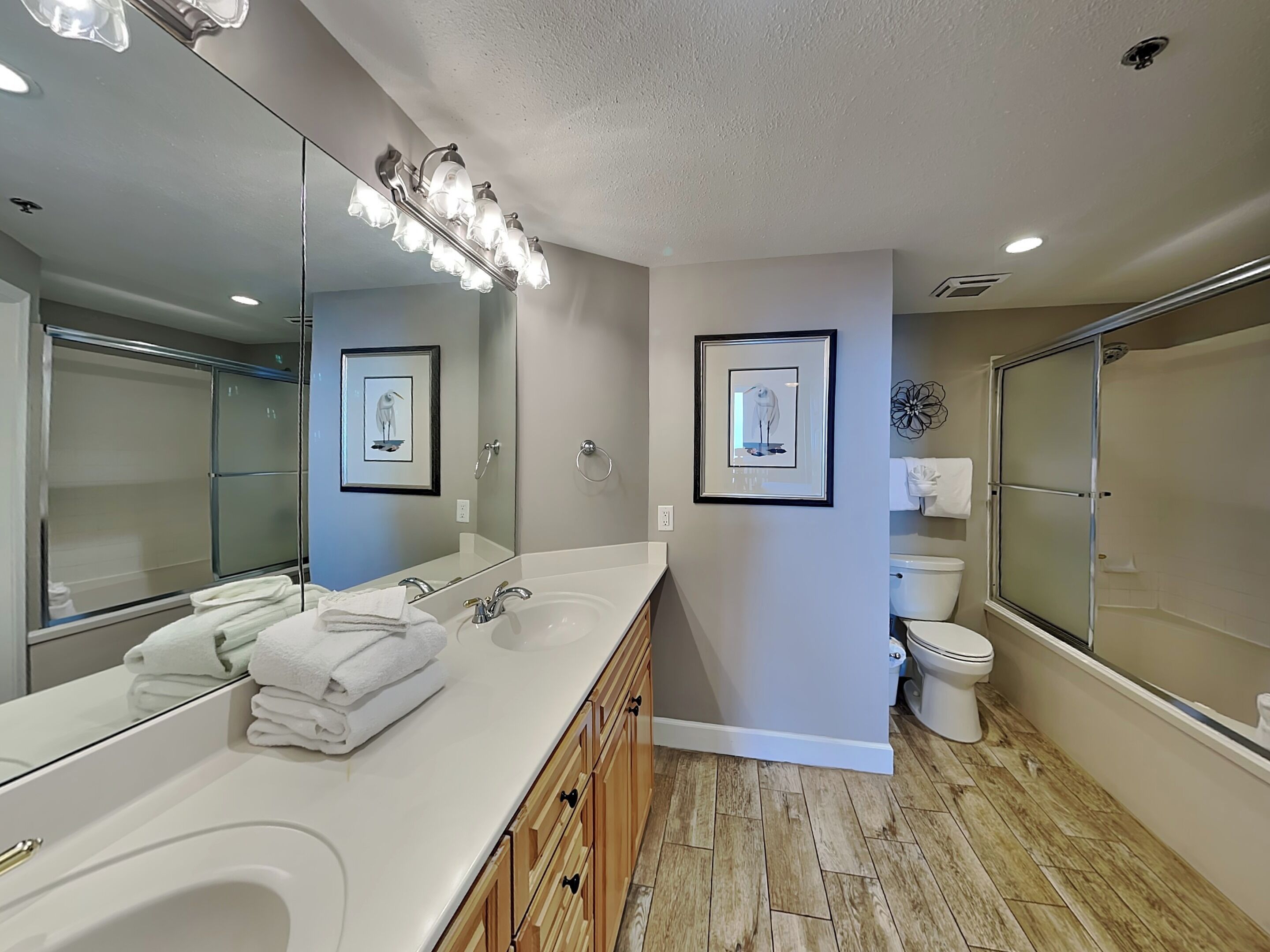 A modern bathroom with a large vanity, a shower enclosure, and two framed wall art pieces.