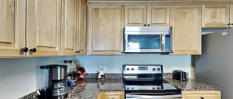 A kitchen with wooden cabinets, a stainless steel microwave, a gas stove, and a coffee maker.