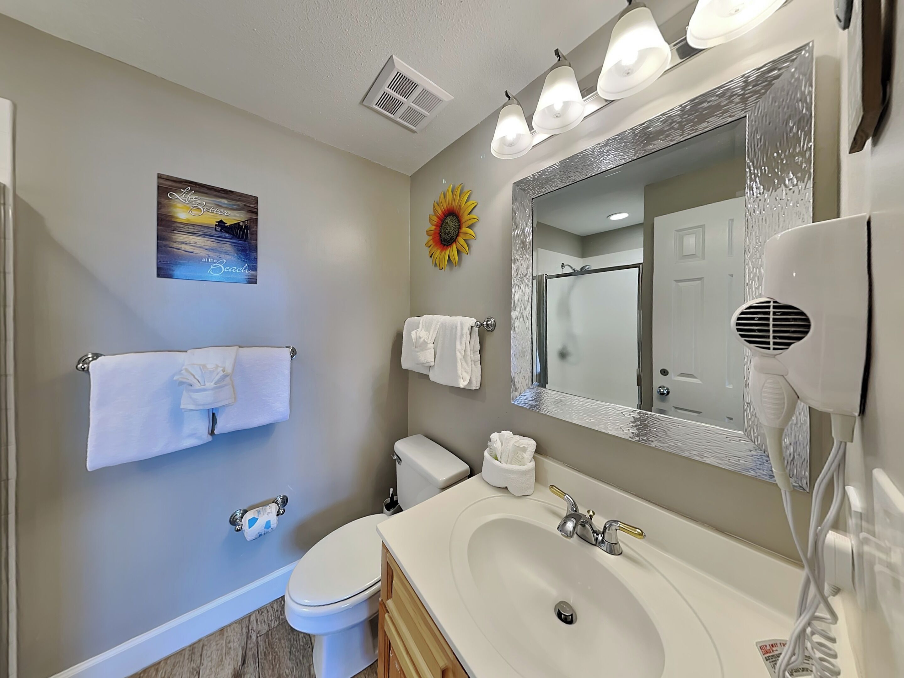 Une salle de bain avec des toilettes, un lavabo et un miroir. Des serviettes sont accrochées au mur, et il y a une décoration représentant un soleil.