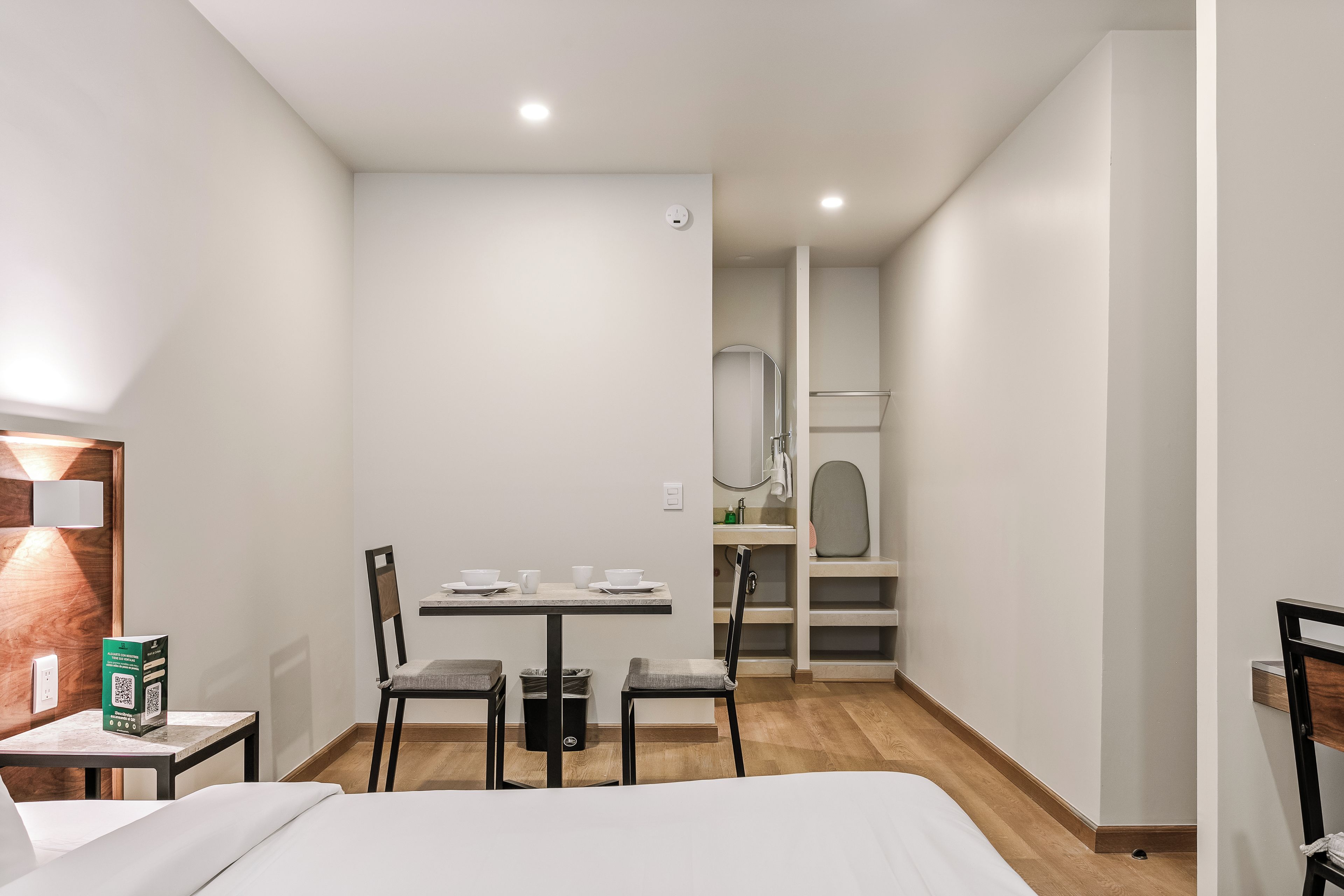 Een hotelkamer met een bed, een tafeltje met stoelen, een bureau en een spiegel.