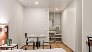 Een hotelkamer met een bed, een tafeltje met stoelen, een bureau en een spiegel.