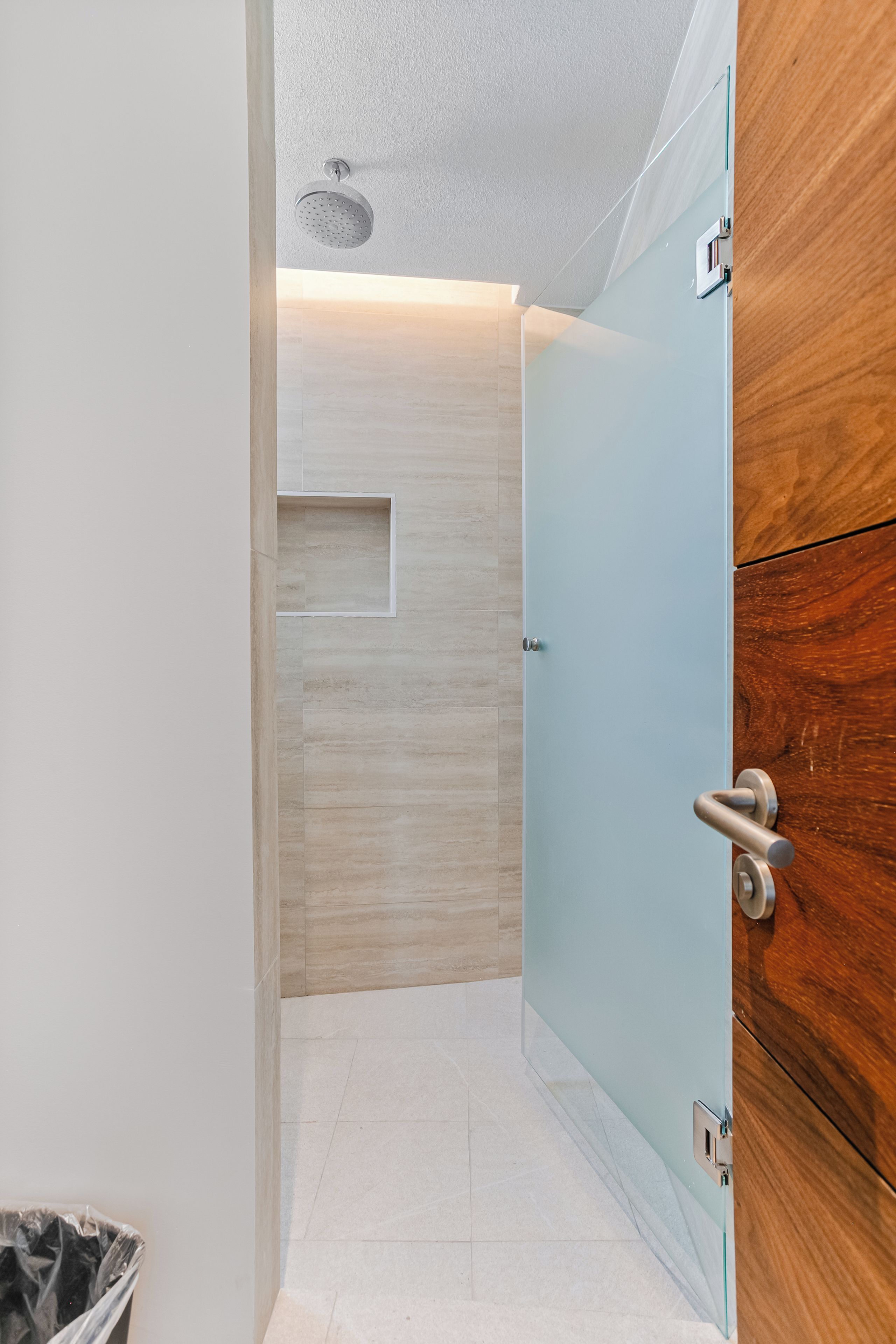 A modern bathroom with a glass shower enclosure, a wooden cabinet, and a tiled floor.