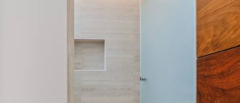 A modern bathroom with a glass shower enclosure, a wooden cabinet, and a tiled floor.
