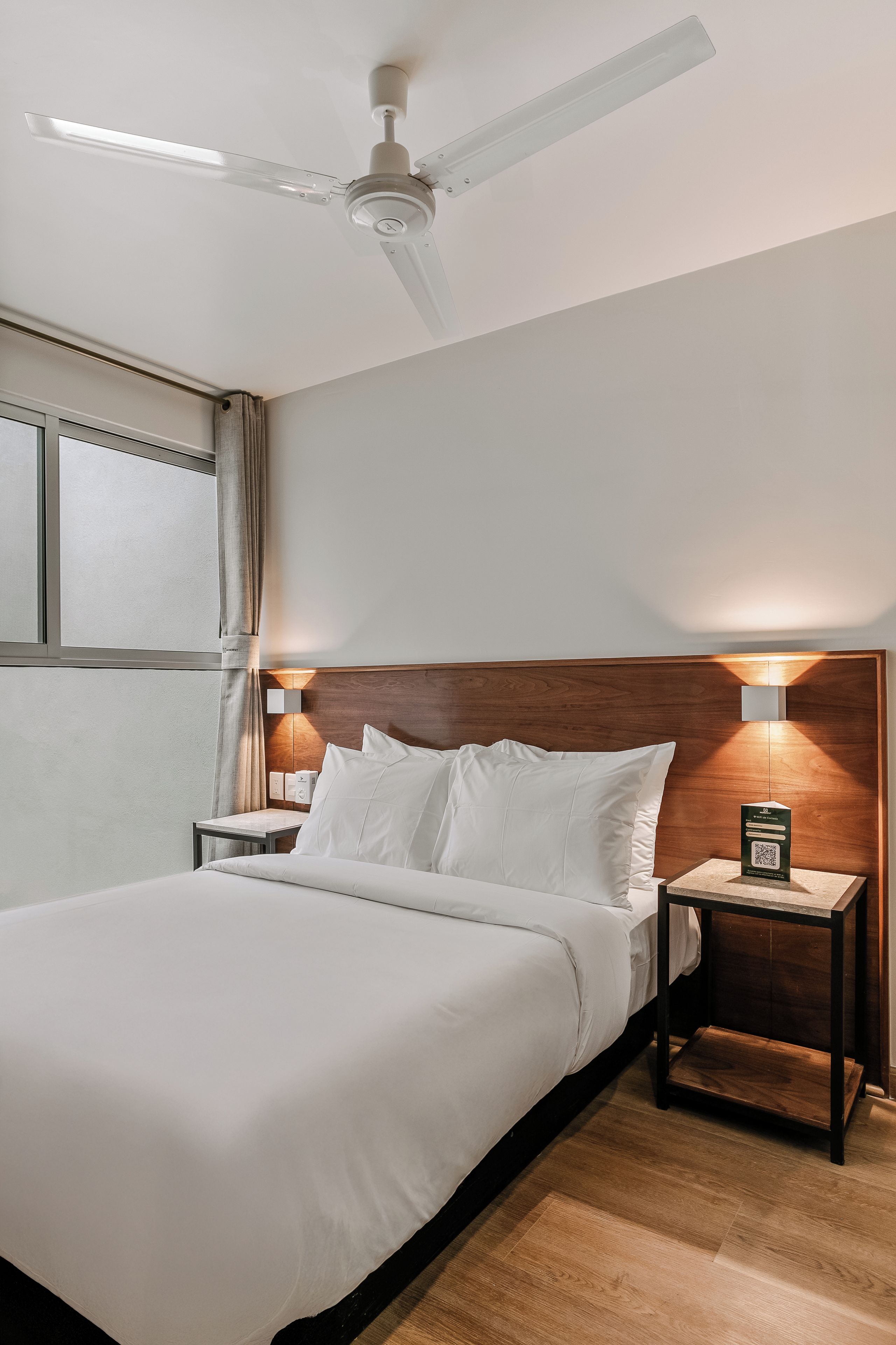 Une chambre d’hôtel équipée d’un lit, de tables de chevet, d’un ventilateur de plafond et d’un luminaire fixé au mur.