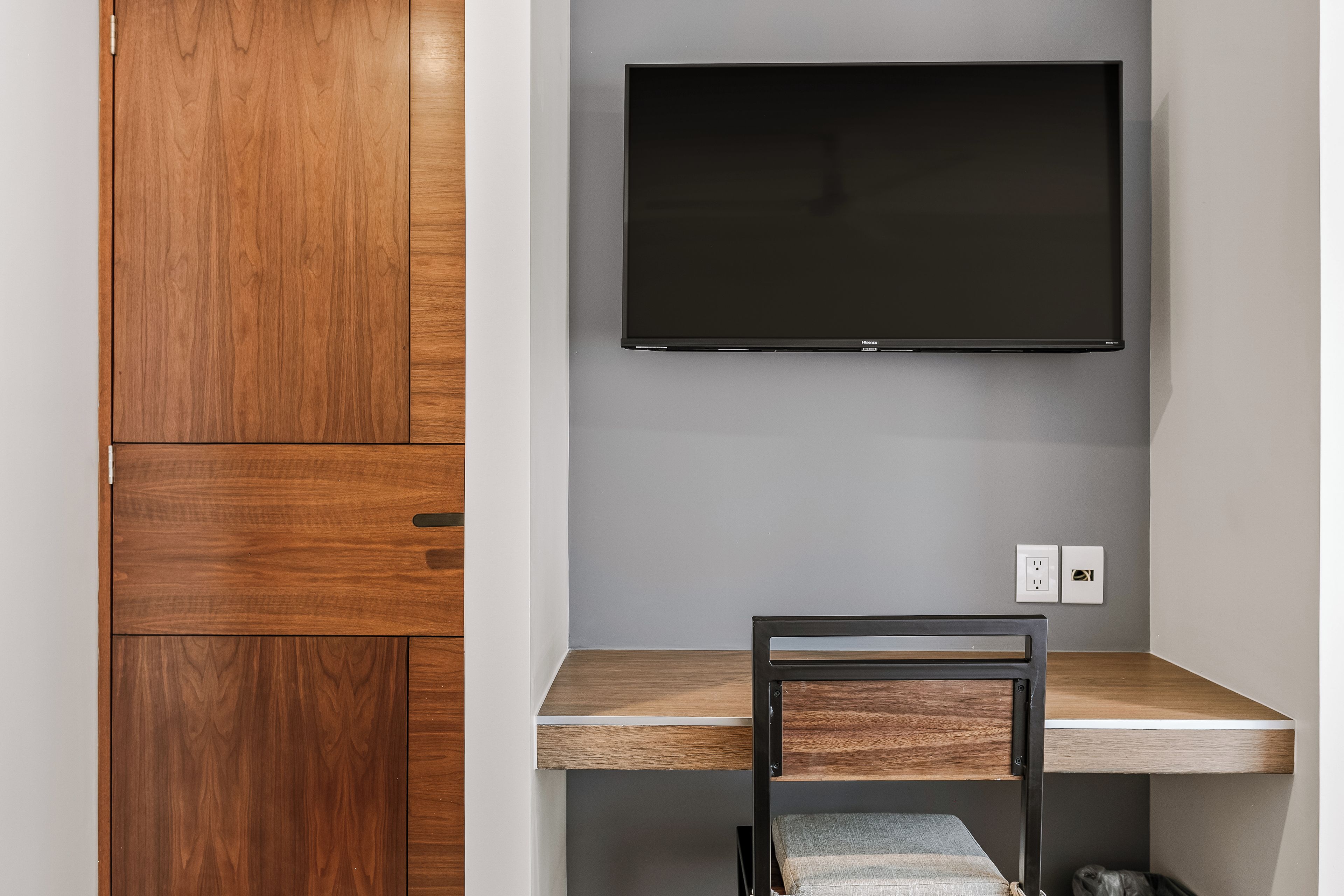 Ein Zimmer mit einem Holzkasten, einem flachbildfernseher an der Wand und einem Schreibtisch mit Stuhl.