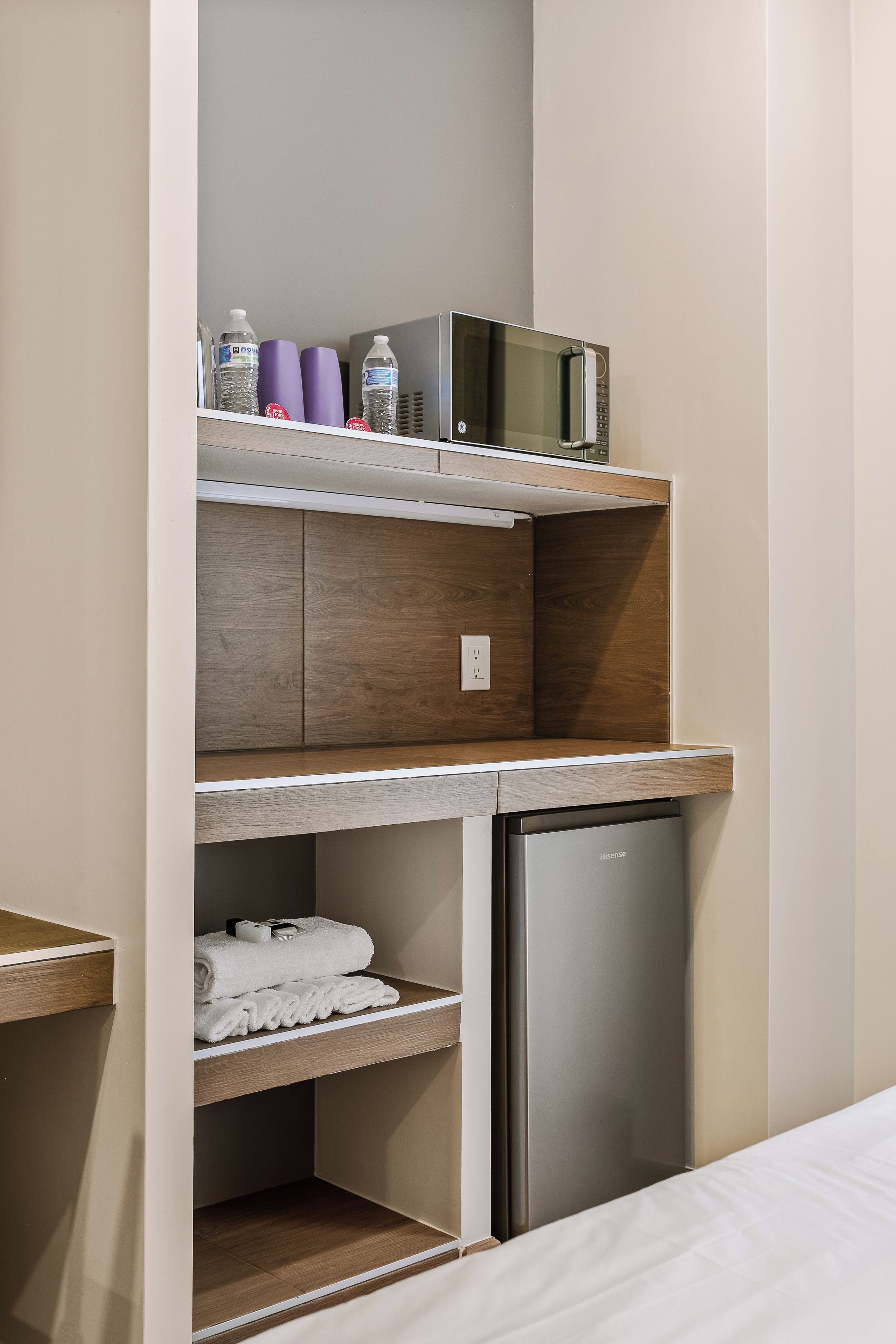 A compact kitchenette with a microwave, water bottles, and a small refrigerator.
