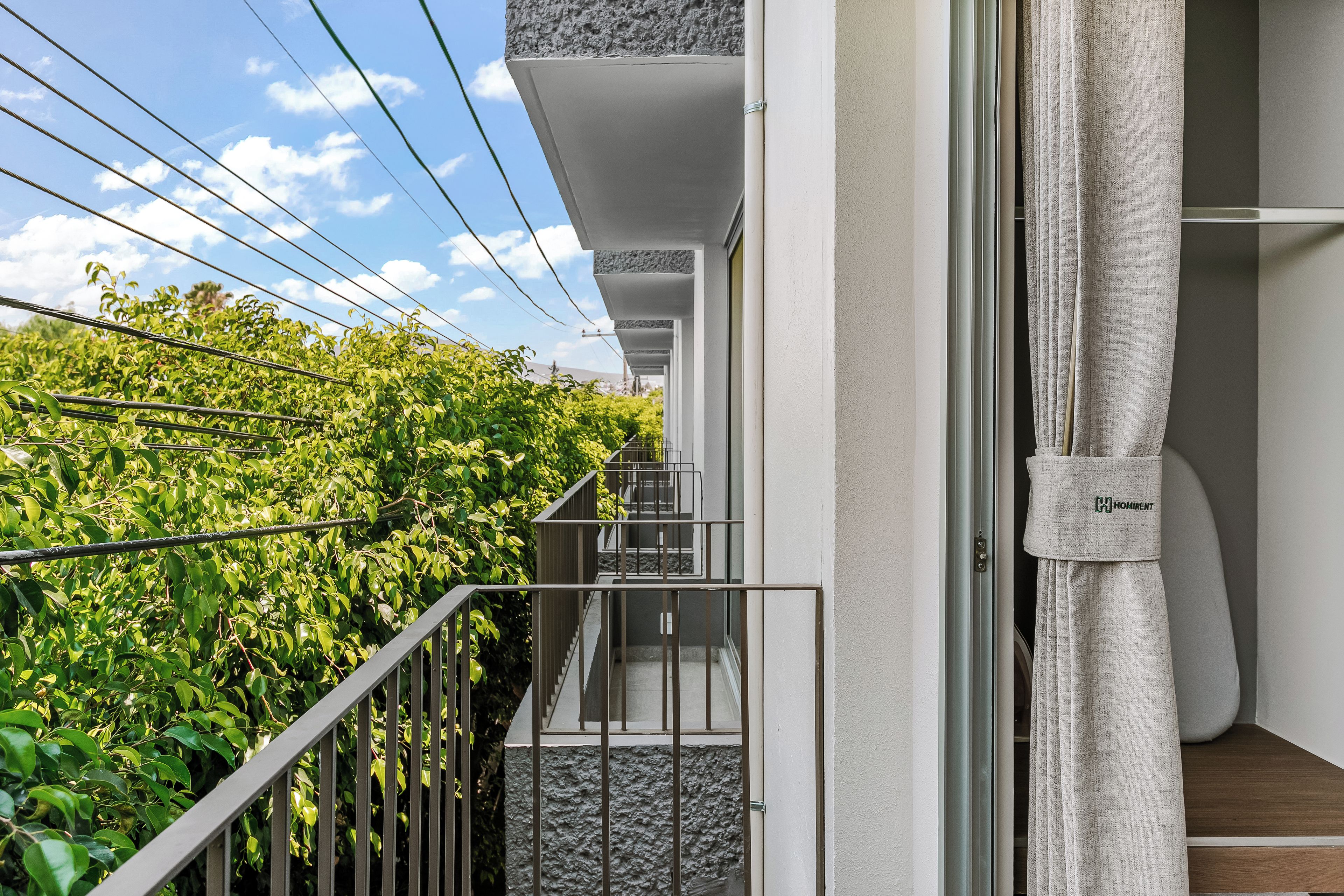 A modern apartment with a balcony overlooking a garden, a staircase, and a view of the sky.