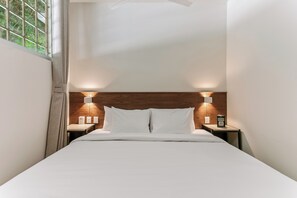 A neatly made bed with white linens, two bedside tables with lamps, and a wooden headboard.