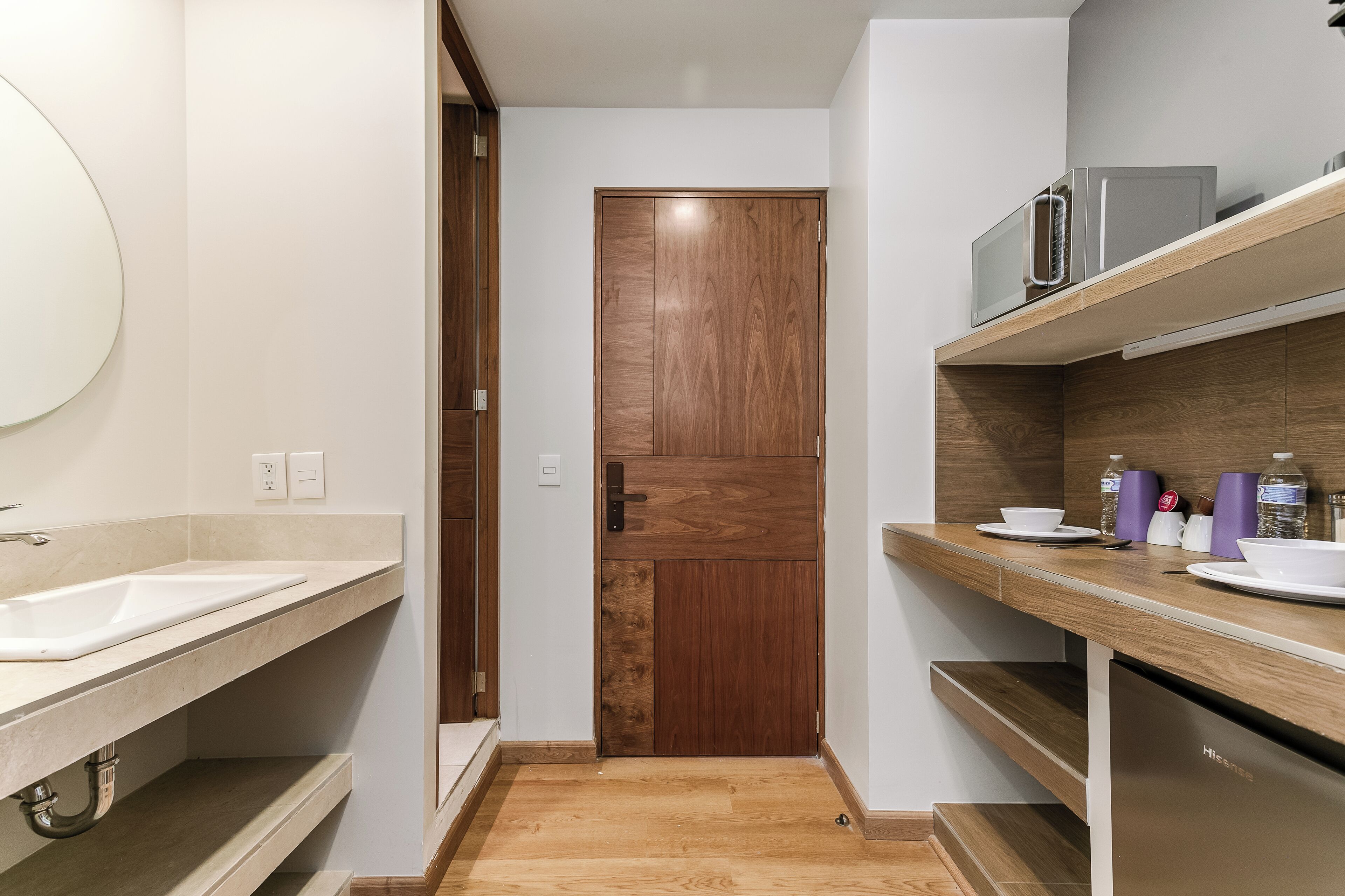 Une petite cuisine avec une porte en bois, un évier et un four à micro-ondes posé sur une étagère.