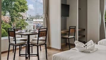 Ein Hotelzimmer mit einem Bett, einem Esstisch mit Stühlen, einem an der Wand montierten Fernseher und Blick auf die Stadt durch das Fenster.