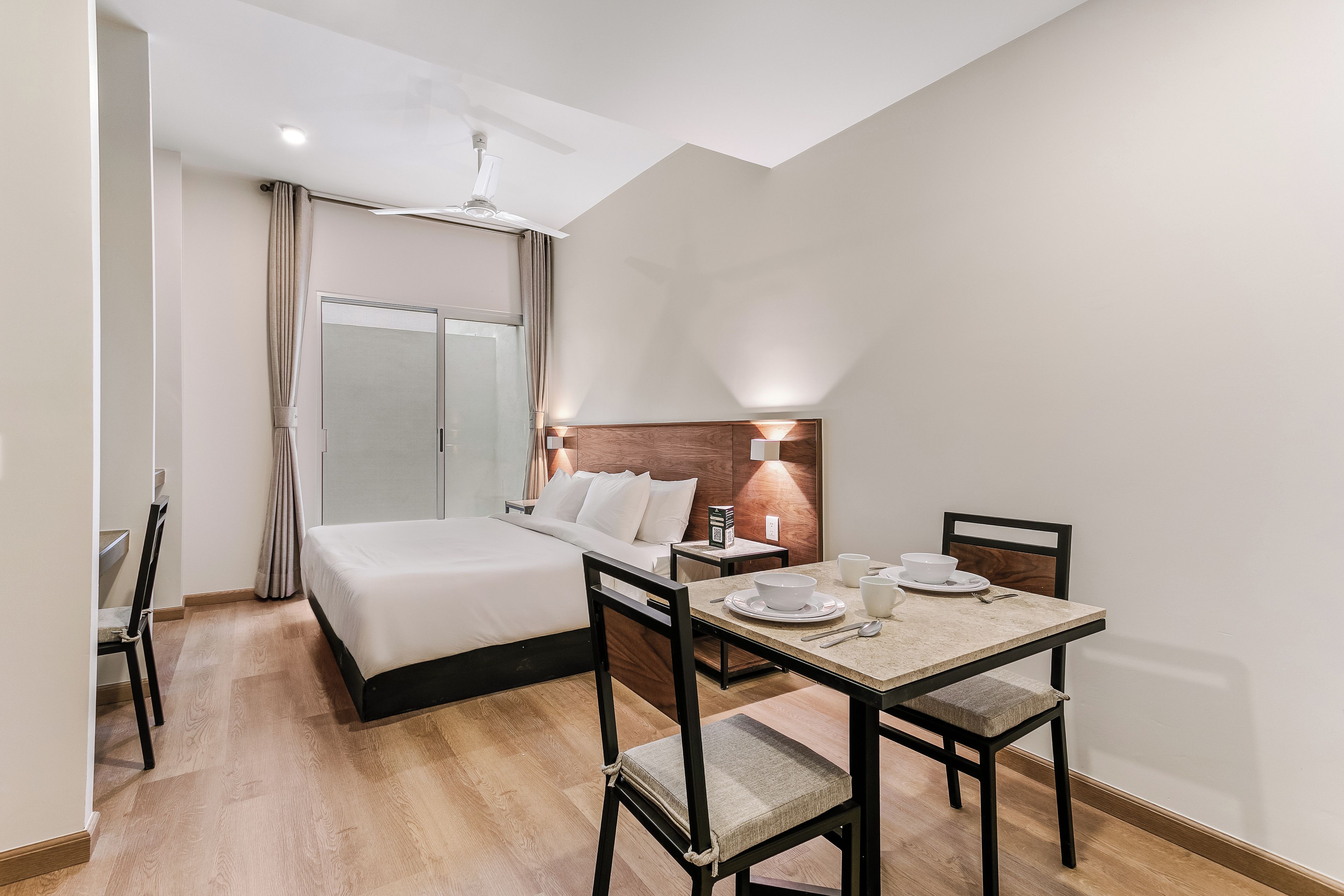 Una habitación de hotel con una cama, una mesa de comedor con sillas, una mesita de noche y una lámpara.