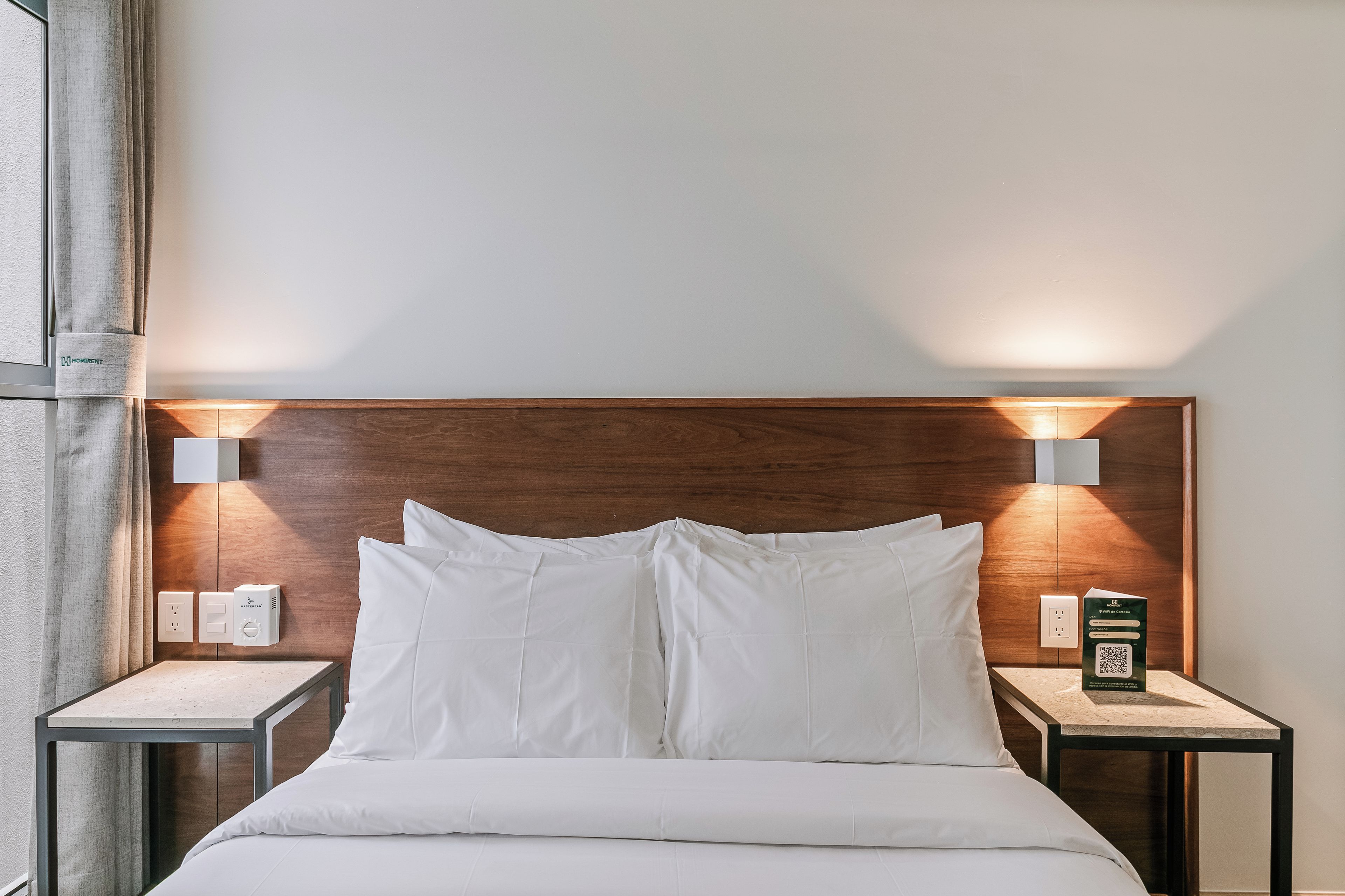 A hotel room with a wooden headboard, two bedside tables with lamps, and a bed with white bedding.