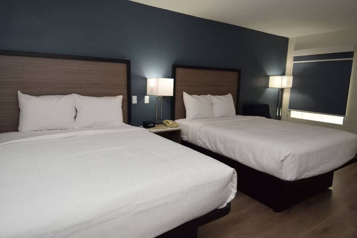A hotel room with two beds, each with a wooden headboard, white bedding, and bedside lamps.
